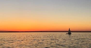 A sailboat gracefully sails in the ocean at sunset, embodying the serenity and beauty of Ageless Societies.